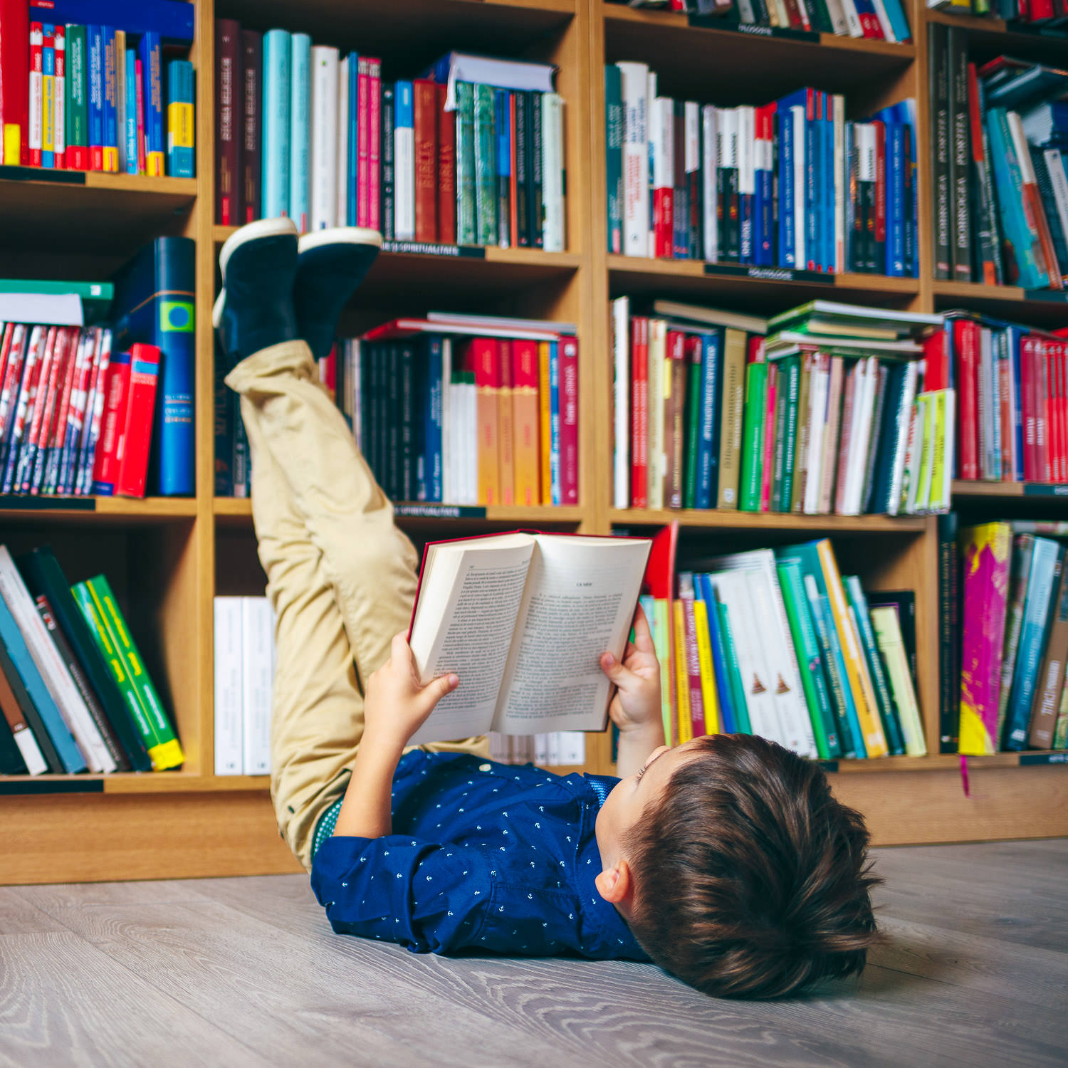 Small boy lying on the floor of a library enjoying a book